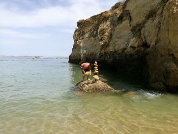 Full length of shirtless man stacking rocks amidst sea