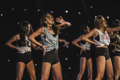 Midsection of friends dancing against black background