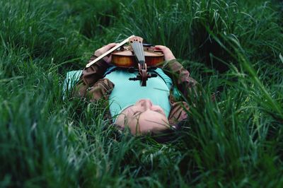 Woman holding violin lying on grassy field