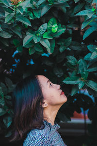 Side view of mid adult woman looking away while standing by plants in park