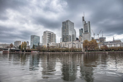 Buildings by river against cloudy sky