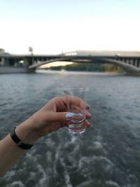 Close-up of hand holding drinking water against river