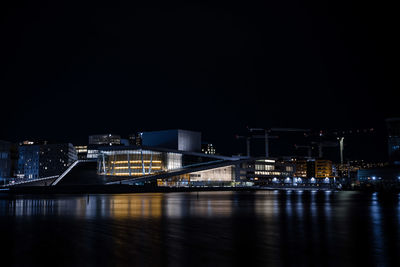 Illuminated buildings by river against sky at night