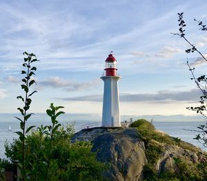 Lighthouse amidst plants and buildings against sky