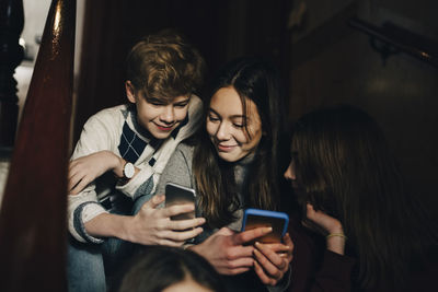 Smiling teenage boy showing mobile phone to female friends while sitting on steps