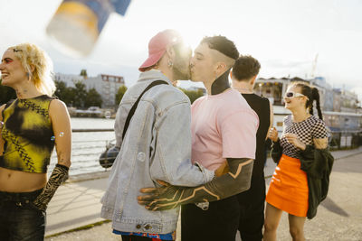 Affectionate gay man kissing non-binary person on promenade in city