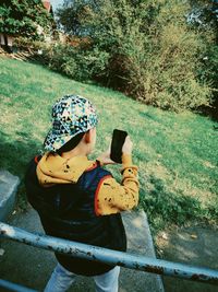 Rear view of woman holding hat against trees