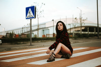 Young woman sitting on road against sky
