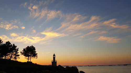 Silhouette buildings by sea against sky during sunset