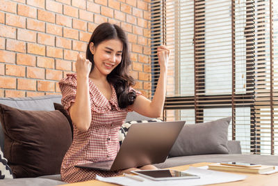 Young woman using phone while sitting on laptop