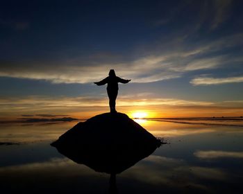 Silhouette woman standing on rock over sea against sky during sunset