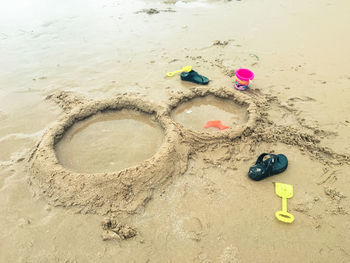 High angle view of toys and flip flops by sand castle at beach
