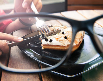 Cropped hands having dessert at table seen through eyeglasses