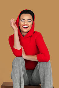 Portrait of young woman sitting against yellow background