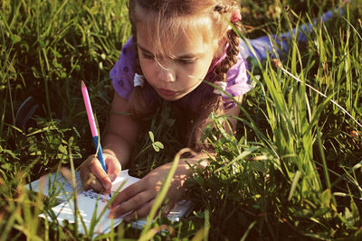 Cute girl writing in diary while lying on grass