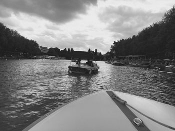 Boats in calm lake against cloudy sky