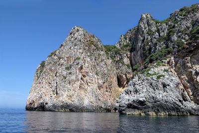 Rock formations in sea against clear blue sky