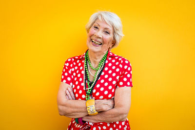 Portrait of smiling senior woman standing against yellow background