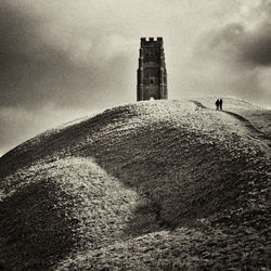 Man walking on field by lighthouse against sky