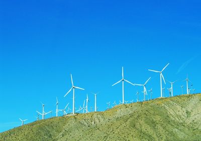 Wind turbines on field against clear blue sky