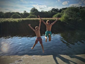 Full length of shirtless friends jumping in lake