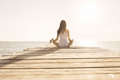 Woman sitting on wooden jetty against sea against clear sky