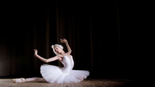 On the stage of the old theater hall. young ballerina in suit of white swan and pointe shoes