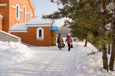 Rear view of women walking on snow covered building