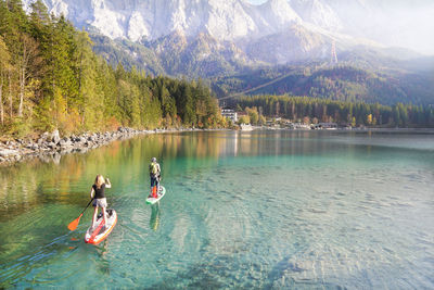 Man and woman rowing boat in lake against mountains