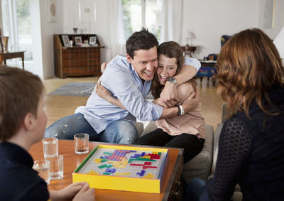 Father hugging daughter while mother and son watching during a match of board game