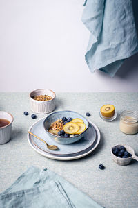 Delicious granola with blueberries and slices of kiwi on ceramic plate near cup of hot tea for breakfast in morning