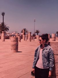 Young woman looking away while standing by stone wall against sky