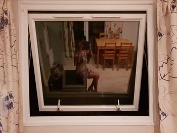 Senior woman taking selfie with digital tablet reflecting on window at home