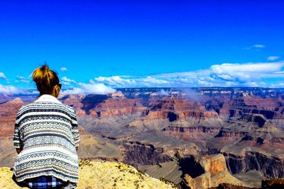 Rear view of woman looking at grand canyon against blue sky