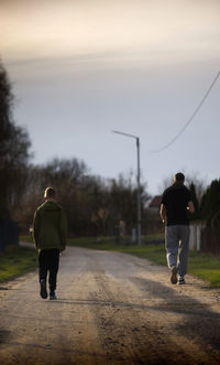 Rear view of man walking on road against sky during sunset