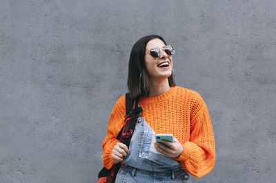 Young woman looking away while standing against wall