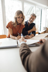 Happy mature woman signing contract with real estate agent at table