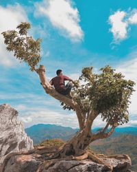 Man sitting on rock against sky