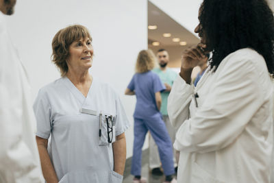 Smiling female doctor with hands in pockets discussing with colleague at hospital