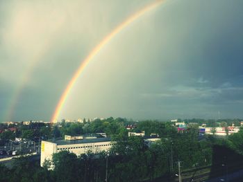 Rainbow over trees against cloudy sky