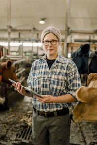 Smiling female farmer standing with tablet pc at cattle farm