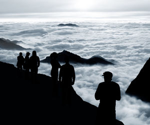 Silhouette people on mountain against cloudscape