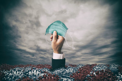 Digital composite image of hand holding umbrella against dramatic sky