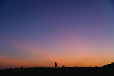 Silhouette people on field against clear sky during sunset