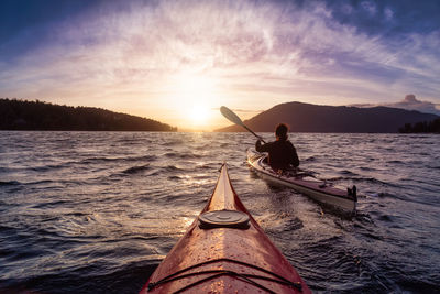 Silhouette man on boat in sea against sky during sunset