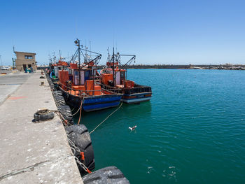 Boats moored at harbor against clear sky