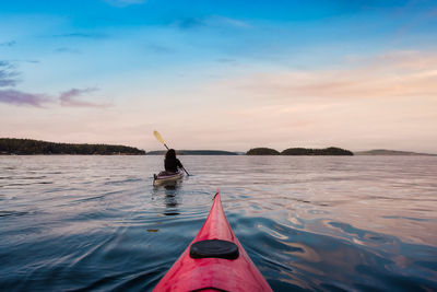 Man on boat in sea against sky during sunset