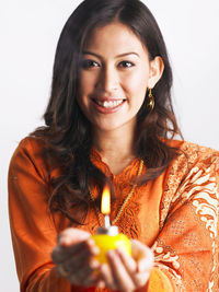 Close-up portrait of smiling young woman holding oil lamp against white background