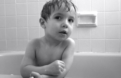 Shirtless boy in bathtub against wall at bathroom