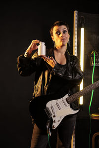 Portrait of young woman playing guitar against black background